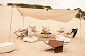 Table, seat cushion and butterfly chairs under shade sail in the sand