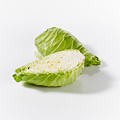Pointed cabbages, whole and halved, on a white surface
