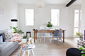 Graues Sofa und alter Holztisch mit Stühlen in offenem Wohnraum mit weißen Wänden