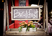 A 'breakfast' sign with flowers on a wooden rack in a restaurant