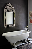 Free-standing bathtub below mirror on dark grey wall