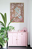 Pop art picture above pink cabinet and houseplants