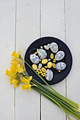 Easter eggs painted blue and white, yellow sugar eggs and marzipan eggs on plate next to narcissus