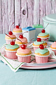 Cupcakes im Retrolook mit pastellfarbener Zuckerglasur und Belegkirschen