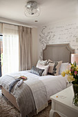 Double bed against wallpaper with pattern of French writing in elegant bedroom with feminine ambiance