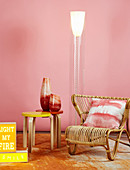 Rattan easy chair, designer standard lamp and vases on side table in front of pink wall