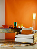 Wood-framed armchair, designer standard lamp and glass vases on console table against orange wall