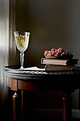 Stillleben mit Weissweinglas, Büchern und Trauben auf antikem Beistelltisch