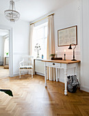 Table with drawer and chair in corner of period apartment with herringbone parquet floor and white walls