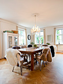 Wooden table and classic chairs with sheepskin rugs in dining room with herringbone parquet floor