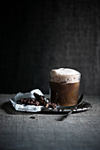 Iced coffee with foamed chocolate soya drink served with dark chocolate and popped oats