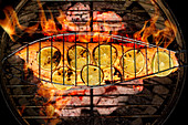 Salmon fillet with lime slices in a fish grilling basket over a charcoal grill