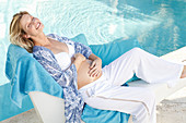 A pregnant woman by the edge of a pool wearing an open blouse