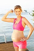A pregnant woman on a jetty wearing a pink sports bra and shorts