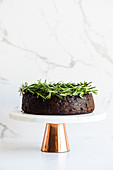 Vegan fruit cake decorated with rosemary sprigs on a cake stand
