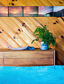 Chest of drawers in front of wooden wall with picture collection in bedroom, turquoise bed linen in foreground