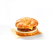 Ein Croissant-Burger mit Käse und Ei vor weißem Hintergrund