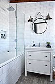 Vanity unit next to bathtub with shower screen in white tiled bathroom