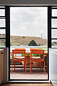 Orangefarbene Stühle am Tisch auf dem Balkon vor Wolkenhimmel