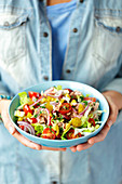 A woman holding a bowl of tuna salad with kidney beans and cherry tomatoes