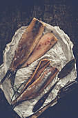 Herring fillets with chives and pink pepper on parchment paper with a knife and fork