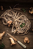 Pfifferlings-Pasta, roh, mit Pfifferlingen, Petersilie und Messer auf Holzuntergrund