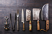 Vintage Butcher meat cleavers, corkscrew and tongs on dark burned wooden background