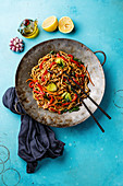 Udon stir fry noodles with oyster mushrooms and vegetables in wok pan on blue background