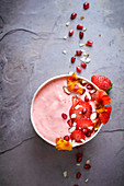 Bowl of strawberry yogurt with fresh sliced strawberries, pomegranate seeds and almonds on a textured stone surface