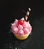 A Shirley Temple cupcake decorated with a cocktail cherry