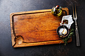 Wooden cutting board background with seasoning, herbs and kitchen fork
