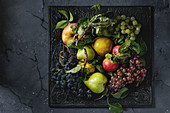 Variety of autumn fruits ripe organic apples, three kind of grapes, pears with leaves on metal ornate tray over dark texture background