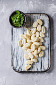 Raw uncooked potato gnocchi on white wooden chopping board with ingredients