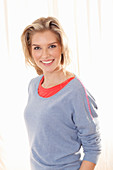 A young blonde woman wearing a blue jumper over a red top