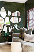 Wooden side tables and scatter cushions on sofa below mirrors on wall with crocodile-effect wallpaper