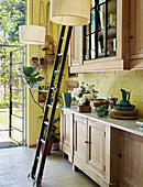 Ladder in front of glass-fronted wall units in country-house kitchen