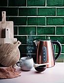 Wasserkocher und eine dampfende Tasse vor grünen Fliesen