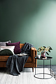 Brown sofa with pillows and plaid against an empty green wall