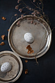 Dried flowers around speckled eggs on two pewter plates
