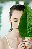 A young woman covering her face with a large leaf
