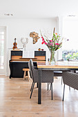 Long, colourful table and grey chairs in front of piano and stool in open-plan interior