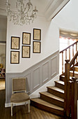 Chair at foot of staircase with panelled wainscotting and gallery of botanical illustrations