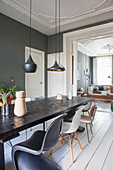 Long dining table and classic chairs in dining room with dark wall and white wooden floor