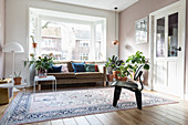 Cushions on sofa in window bay, houseplants and rug in bright living room