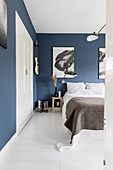 Double bed in bedroom with blue wallpaper, large artworks and white wooden floor