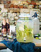 Cold ginger beer and gin punch with cucumber and lime in a drink dispenser