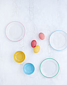 Coloured Easter eggs between empty plates and bowls (seen from above)