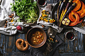 Herbstlich gedeckter Tisch mit Gemüsesuppe, Ofengemüse, Brezeln und Rotwein