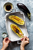 Hands brushing eggplants with olive oil, preparing eggplant for roasting