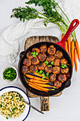 Gluten-Free Honey Garlic Meatballs and roasted baby carrots in a cast iron pan placed on a wooden cutting board